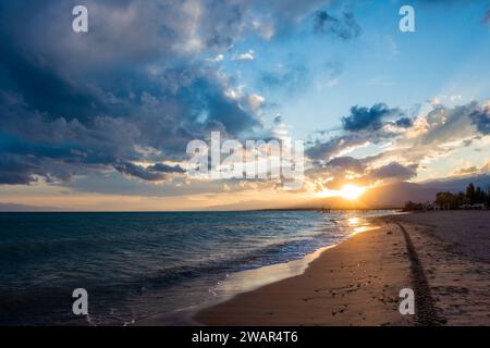 Farbenfroher Sonnenuntergang auf dem Meer. Bergsee in den Strahlen der orangen Sonne. Kirgisistan, Issyk-Kul-See. Natürlicher Hintergrund. Querformat Stockfoto