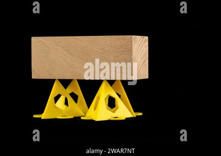 Holzblock, der auf gelben stapelbaren Malern gestützt wird, zeigt Pyramidendreiecke isoliert auf schwarzem Hintergrund Stockfoto