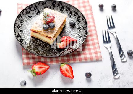 Ein Stück Napoleonkuchen mit Mohnsamen und Kirschen, dekoriert mit Erdbeeren und Blaubeeren auf hellem Hintergrund. Schließen Stockfoto