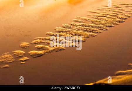 Ein abstraktes Bild eines wunderschönen Sonnenuntergangs mit einem orangefarbenen Himmel mit Fußabdrücken im Sand Stockfoto