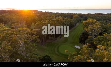 Eine atemberaubende Luftaufnahme eines Golfplatzes bei Sonnenaufgang mit üppigem grünem Gras, hohen Bäumen und einem wunderschönen goldenen Himmel Stockfoto