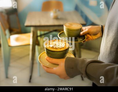 Zwei Personen stehen an einem Tisch, vor ihnen stehen zwei Kaffeetassen, jede auf einem eigenen Teller Stockfoto