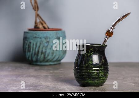 Schwarz-grüner Yerba Mate Becher mit einer Topfpflanze im Hintergrund, leerer Platz für Text Stockfoto