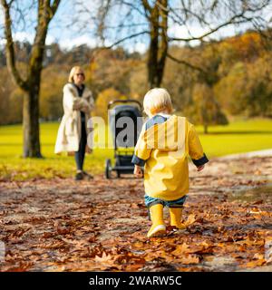 Die Sonne scheint immer nach dem Regen. Kleiner Junge aus Bond mit gelben Gummistiefeln und gelbem wasserdichtem Regenmantel, der an sonnigem Regentag in Pfützen und Herbstlaub im Stadtpark spaziert Stockfoto