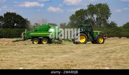 John Deere 6155R-Traktor mit einer L1534-Ballenpresse in der Landschaft von Wiltshire an einem sonnigen Sommertag. Stockfoto