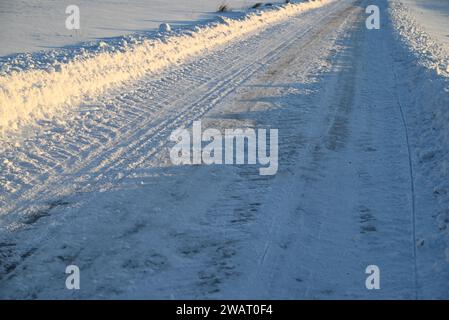 Schneebedeckte, vereiste Landstraße, gesäumt von Schneewehungen an einem sonnigen Wintertag. Stockfoto