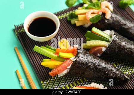 Bambusmatte mit leckeren Sushi-Zapfen und Sojasoße auf farbigem Hintergrund, Nahaufnahme Stockfoto