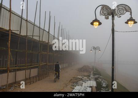 Ein Mann fährt an einem nebeligen Morgen mit dem Fahrrad an einer Baustelle vorbei, bevor der indische Premierminister Narendra Modi in Ayodhya besucht. Ramnagari Ayodhya, einst bekannt für seine engen Gassen und verfallenen Straßen, macht stetige Fortschritte: Alle Straßen und Gebäude, die zum RAM Janmabhoomi führen, werden erweitert und renoviert, um ein reibungsloses Reisen zu ermöglichen. Stockfoto