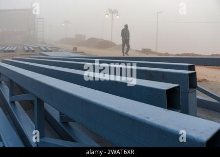 Ayodhya, Indien. Dezember 2023. Ein Mann läuft an einem nebeligen Morgen vor dem Besuch des indischen Premierministers Narendra Modi in Ayodhya an Baumaterialien entlang, die auf einem neu gebauten Bürgersteig gelegt wurden. Ramnagari Ayodhya, einst bekannt für seine engen Gassen und verfallenen Straßen, macht stetige Fortschritte: Alle Straßen und Gebäude, die zum RAM Janmabhoomi führen, werden erweitert und renoviert, um ein reibungsloses Reisen zu ermöglichen. (Credit Image: © Biplov Bhuyan/SOPA Images via ZUMA Press Wire) NUR REDAKTIONELLE VERWENDUNG! Nicht für kommerzielle ZWECKE! Stockfoto