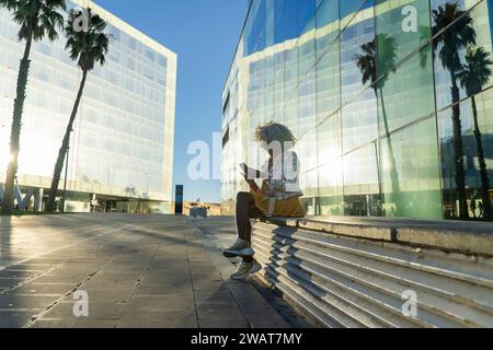 Stilvolle, afro-amerikanische Dame mit gräulichen Afro-Haaren, die am Handy spricht, im modernen Stadtzentrum. Konzept: pro-Aging, Kommunikation Stockfoto