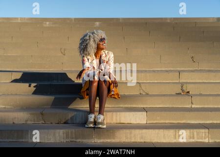 Stilvolle, afro-amerikanische Dame mit gräulichen Afro-Haaren und Sonnenbrille, die sich in der Sonne in urbaner Umgebung entspannt. Konzept: pro-Aging, Urlaub Stockfoto