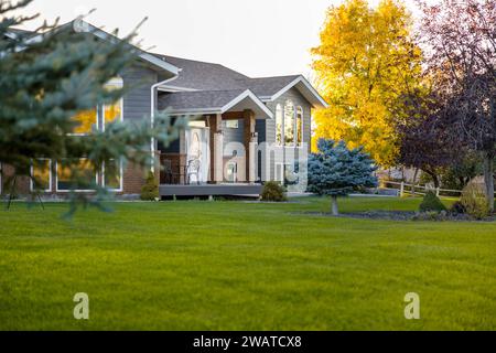 Ein wunderschönes zweistöckiges Haus, umgeben von üppigem grünem Gras und hohen Bäumen im Backyardv Stockfoto