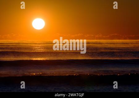 Atlantisches Erwachen: Majestätischer Sonnenaufgang, der ein warmes Orange über die nebligen Wellen des Ozeans wirft Stockfoto