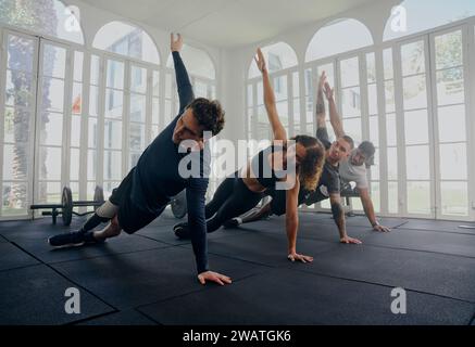Gruppe multirassischer junger Erwachsener in Sportbekleidung, die im Fitnessstudio nebeneinander eine Plank-Pose machen Stockfoto