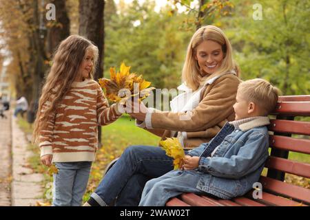 Glückliche Mutter und ihre Kinder verbringen Zeit zusammen mit trockenen Blättern im Herbstpark Stockfoto