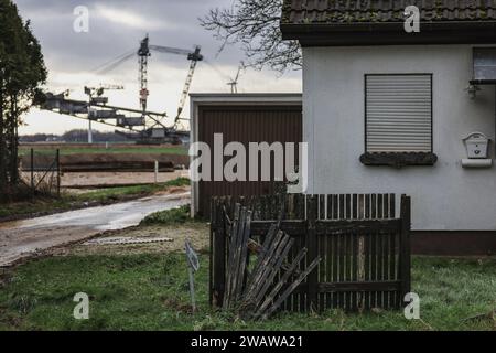 Erkelenz, Deutschland. Januar 2024. Hinter einem verlassenen Haus im Stadtteil Keyenberg steht ein Braunkohlebagger. Die Braunkohlebagger graben weiterhin im rheinischen Bergbaugebiet. Aber die Zeit danach rückt zunehmend in den Fokus. Zum Beispiel, wie man den leeren Dörfern in der Nähe des Tagebaus Leben erweckt. In den Rathäusern werden Konzepte geschaffen. Im Frühjahr könnte es konkreter werden. (Für dpa/lnw: "Pläne für die Zeit nach Kohle: Von zukünftigen Dörfern und neuen Seen") Kredit: Oliver Berg/dpa/Alamy Live News Stockfoto