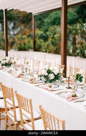 Langer überdachter Festtisch im Garten mit Blumensträußen und Kerzen Stockfoto