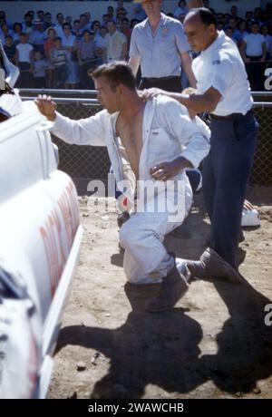 SACRAMENTO, KALIFORNIEN - AUGUST 1958: Eine Gruppe von Männern kümmert sich um den Fahrer, nachdem sein Auto während einer Autoausstellung auf der Sacramento State Fair um den August 1958 in Sacramento, Kalifornien, umgekippt und abgestürzt ist. (Foto: Hy Peskin) Stockfoto