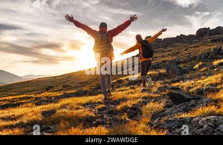 Ein paar Wanderer laufen zusammen in den Bergen des Sonnenuntergangs. Zwei junge Touristen mit Rucksäcken stehen mit offenen Armen und genießen den Sonnenuntergang Stockfoto