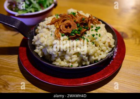 Pongauer Kasnocken Käse Spätzle Pasta in einer Eisenpfanne mit gebratener knuspriger Zwiebel und grünem Salat Stockfoto