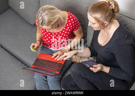 Draufsicht von zwei Frauen, die mit Laptop und Smartphone Waren aus dem Internet auswählen. Stockfoto