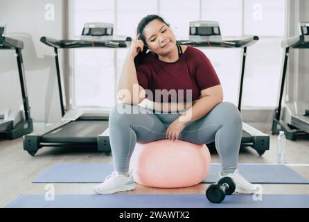 Frauen in Übergröße denken Fragestellung, asiatische fette weibliche, die im Fitness-Studio des Sportclubs sitzt Stockfoto