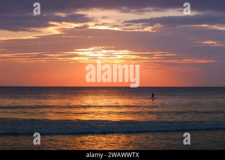 Silhouette eines Mannes auf einem SUP-Board im Meer vor dem Hintergrund eines bunten Sonnenuntergangs. Tropische Insel, Urlaub, aktive Erholung am Meer, Reisen. Stockfoto