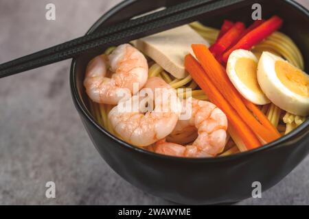 Nudeln mit Gemüse und Garnelen in einer schwarzen Schüssel anbraten. Schieferhintergrund. Draufsicht. Kopierbereich. Mit Zutaten Eier, Tofu, Garnelen Stockfoto