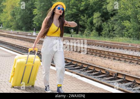 Ein Blick auf morgen: Eine Frau mit einem Koffer in gelber Kleidung und blauer Brille blickt in eine Zukunft voller Abenteuer. Zeit zu gehen: Das Bild eines Stockfoto
