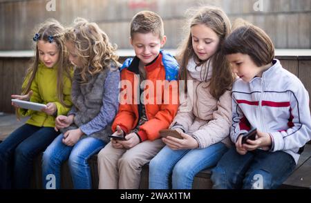 Kinder, die auf der Straßenbank im Park auf Smartphones spielen Stockfoto