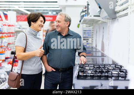 Reifes Paar, das sich für einen Herd in der Haushaltsgeräteabteilung im Lebensmittelgeschäft entscheidet Stockfoto