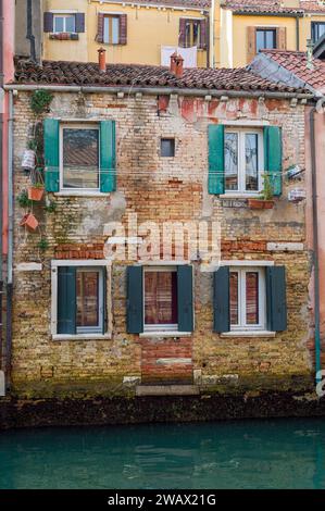 Ein altes, aber charmantes Backsteinhaus an einem kleinen Kanal in Venedig, dekoriert mit ein paar Blumentöpfen. Die Fenster sind mit soliden Fensterläden aus Haus ausgestattet Stockfoto