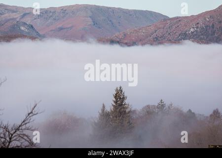 Cumbria, Großbritannien. Januar 2024. Wetter in Großbritannien. Sonnenbrand des tief liegenden Nebels über dem versteckten Lake Windermere, vom Windermere Village aus gesehen, dem Lake District. Quelle: Gordon Shoosmith/Alamy Live News Stockfoto