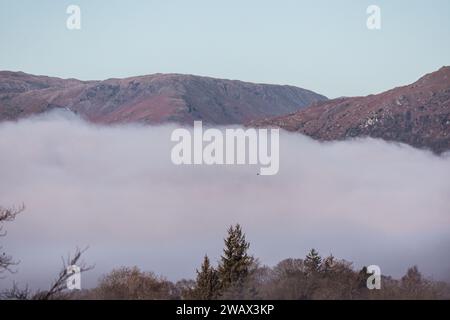 Cumbria, Großbritannien. Januar 2024. Wetter in Großbritannien. Sonnenbrand des tief liegenden Nebels über dem versteckten Lake Windermere, vom Windermere Village aus gesehen, dem Lake District. Quelle: Gordon Shoosmith/Alamy Live News Stockfoto