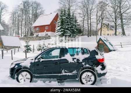 Der schneebedeckte SUV steht in der Nähe eines Holzschuppen im Dorf Stockfoto