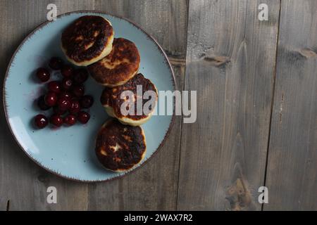 Verbrannte Käsekuchen auf einer blauen Platte auf grauem Hintergrund mit Platz für Text. Hüttenkäsepfannkuchen mit Kirschbeeren Copy Space. Stockfoto