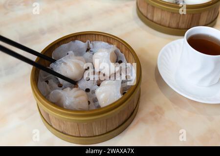 Traditionelles kantonesisches Dim Sum wird mit Essstäbchen aufgefangen - ha Gow (oder har Gow) - Garnelenknödel serviert in einem Bambusdampfer, Großbritannien Stockfoto