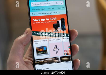 Black Friday Week mit Werbebanner und Seite aus der Amazon Shopping App auf einem Smartphone, das von einer Hand gehalten wird, UK Stockfoto