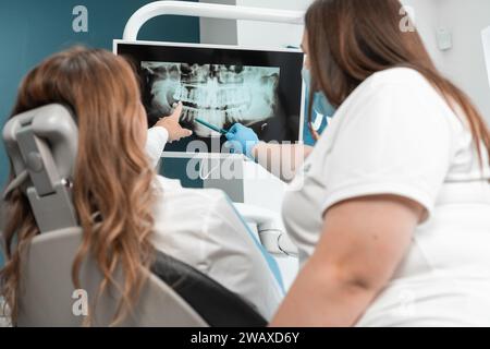 Der Zahnarzt zeigt dem Patienten eine Panorama-Röntgenaufnahme auf dem Monitor und erklärt alle Details und Merkmale ihres Zahnzustands sorgfältig. Ein Zahnarzt Stockfoto