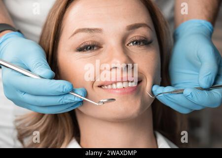 Der Zahnarzt, der die Instrumente hält, behandelt den Patienten selbstbewusst und sorgfältig und bietet einen schmerzfreien und professionellen Ansatz. Frau lächelt mit Stockfoto