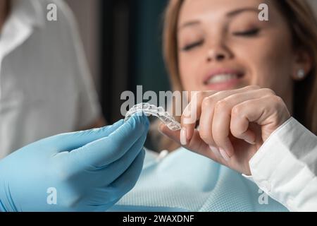 Aufmerksamer Zahnarzt, der Aligner-Aligner in den Händen demonstriert, weibliche Patientin in der Zahnarztpraxis zeigt, sich auf die Arbeit vorbereitet und sich bemüht, den zu machen Stockfoto