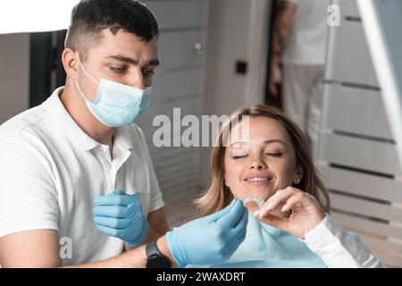 Der Zahnarzt hält Aligner-Aligner in der Hand, bereitet sich auf wichtige Behandlungsstufen vor und bietet dem Patienten Komfort. Erläutert und demonstriert die Vorteile Stockfoto