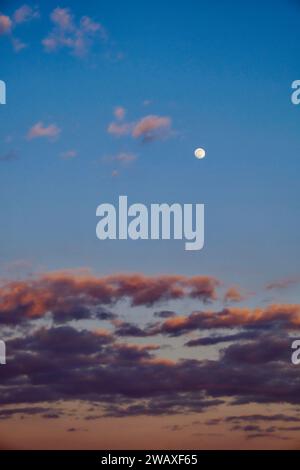 Ein klarer Abendhimmel mit sichtbarem Mond, umgeben von dunklen Wolken. Stockfoto