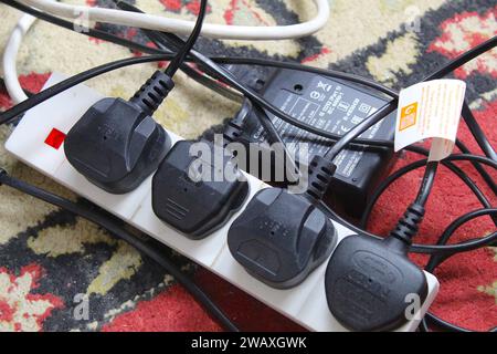 Dublin, Irland - 3. Januar 2024: Ein Foto einer Reihe schwarzer Stecker, die in einen elektrischen Verlängerungsstecker auf dem Teppichboden gesteckt wurden. Stockfoto