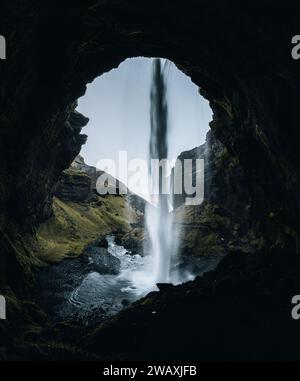 Kvernufoss Wasserfall in der Bergschlucht. Touristenattraktion Island. Mann in roter Jacke steht und schaut auf den Fluss des fallenden Wassers Stockfoto