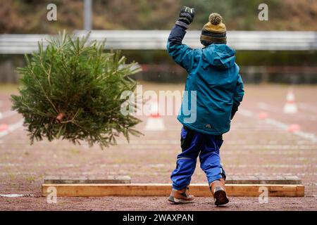 Weidenthal, Deutschland. Januar 2024. Ein Kind wirft eine Fichte bei der 16. Weihnachtsbaumwurfweltmeisterschaft. Die vom FC Wacker Weidenthal gegründete „Weltmeisterschaft“ findet in einem drei-Wege-Wettbewerb statt: Langwurf, Hochwurf und Schleudern eines Baumes von etwa 1,50 Metern. Quelle: Uwe Anspach/dpa/Alamy Live News Stockfoto