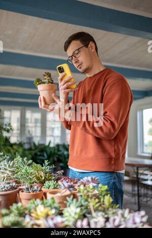 Junger Mann, der die Pflanze im Geschäft wählt, indem er Fotos macht und Informationen in mobilen Anwendungen liest Stockfoto