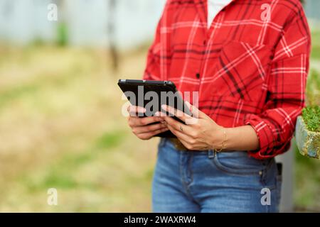 Zugeschnittenes Bild einer multiethnischen Landwirtin im Gewächshaus, die Tablette hält. Stockfoto