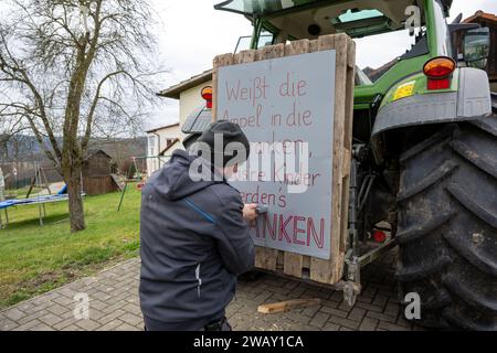 07. Januar 2024, Bayern, Wüstenwelsberg: Ein Mann bringt ein Protestschild mit der Aufschrift "Stelle die Ampel, unsere Kinder werden uns danken" an einen Traktor. Die Landwirte bereiten sich auf die kommende Aktionswoche vor. Tausende von Landwirten wollen gegen die Agrarpolitik demonstrieren. Foto: Pia Bayer/dpa Stockfoto