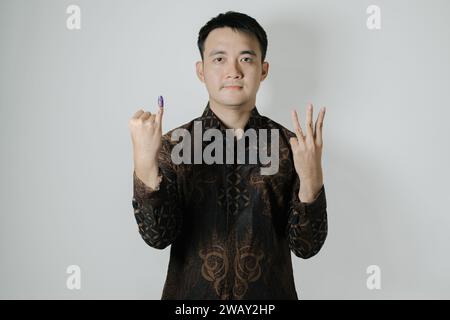 Asiatischer Mann mit Batiktuch zeigt seinen kleinen Finger mit violetter Tinte und wählt nach Pemilu oder Indonesien die Nummer drei Stockfoto